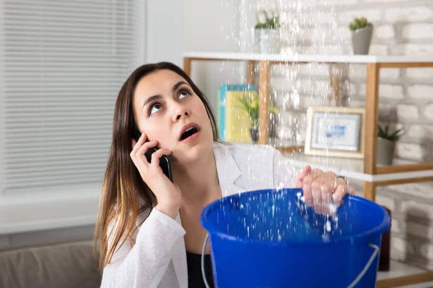 Femme inquiète appelant plombier recueillant des gouttelettes d'eau qui fuient du plafond