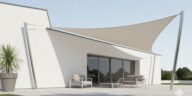 villa avec un voile d'ombrage blanc en forme de triangle étendu sur le côté de la maison pour fournir de l'ombre sur le patio